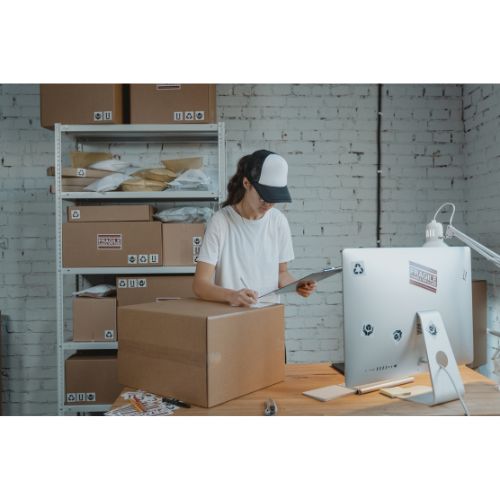 Person packar lådor på kontor med hyllor.