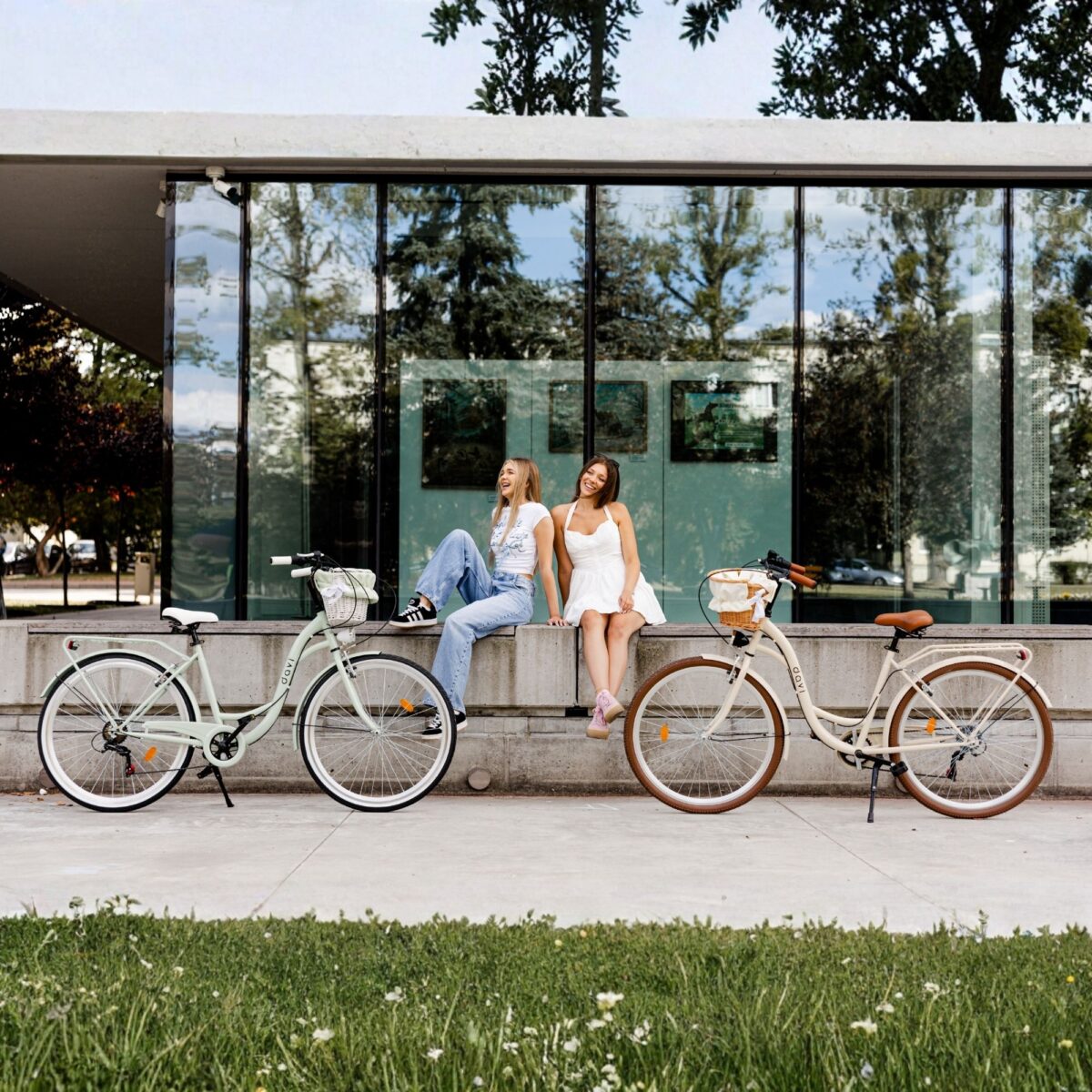 Två kvinnor sitter nära cyklar utanför byggnad.