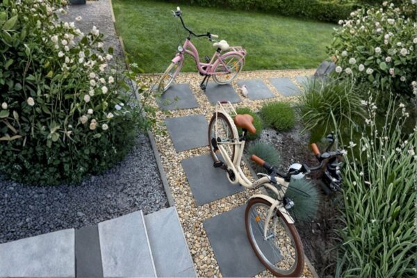 Två cyklar i en trädgård med stengång.